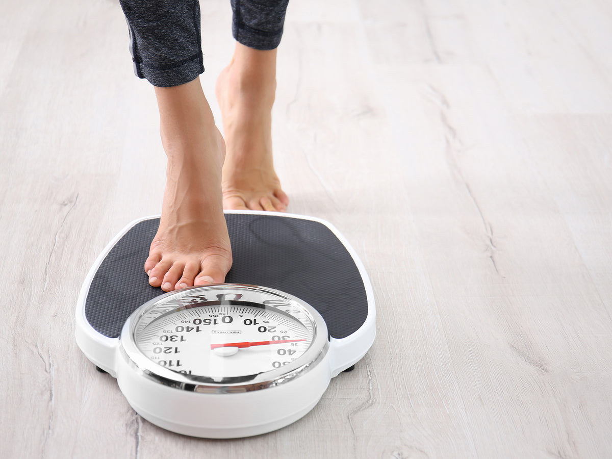 Close-up of a person stepping on a traditional analog weighing scale, suggesting body weight tracking or monitoring as part of a health or weight loss routine.