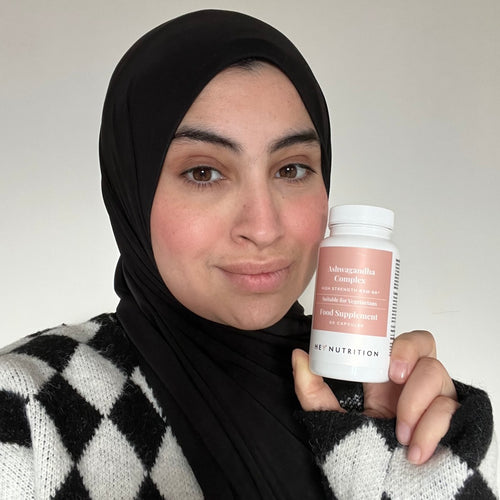 Woman wearing a black hijab and patterned sweater, holding a bottle of Hey Nutrition Ashwagandha Complex close to her face.